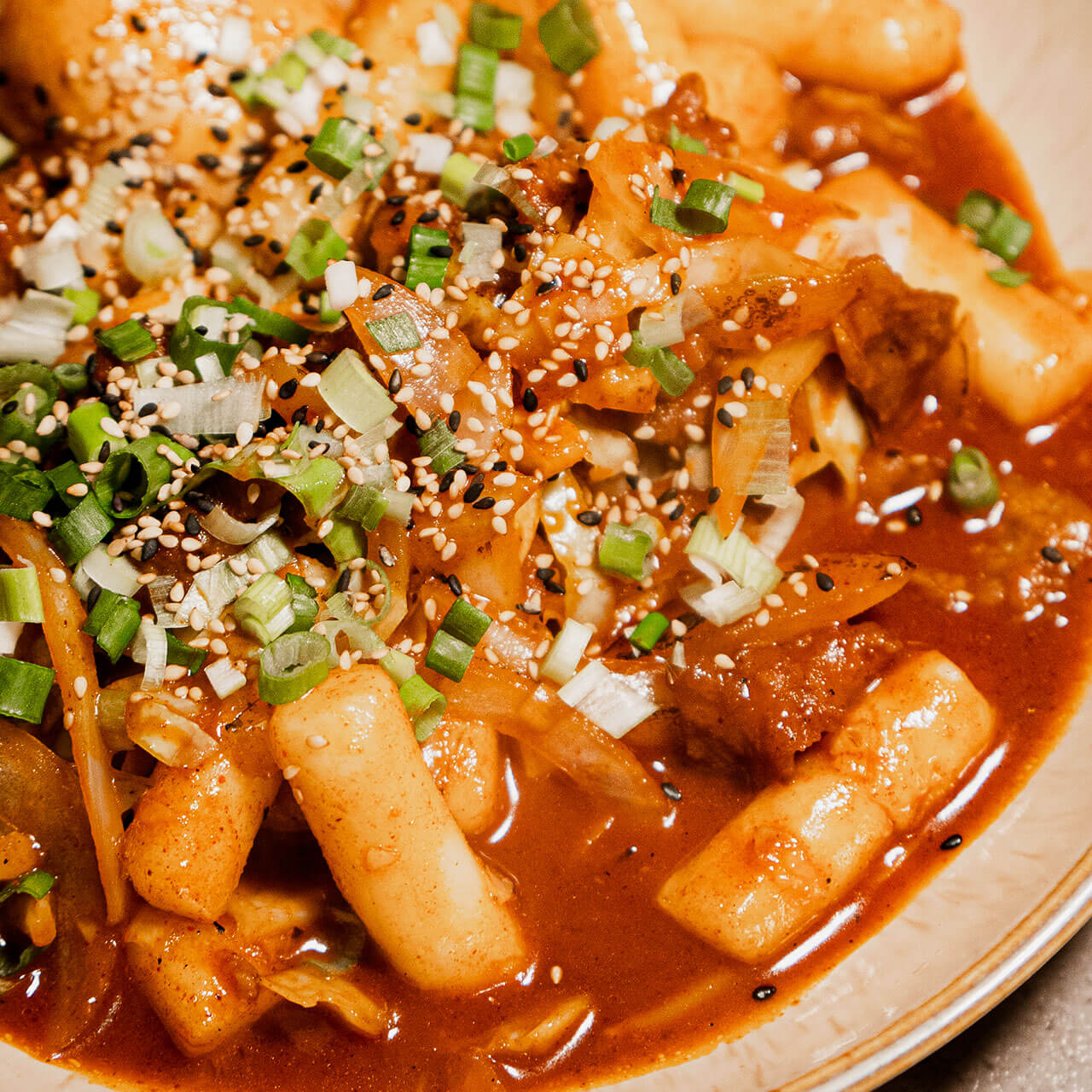 A Korean street-food classic featuring chewy rice cake in a sweet and spicy sauce, enjoyed by people from all walks of life.