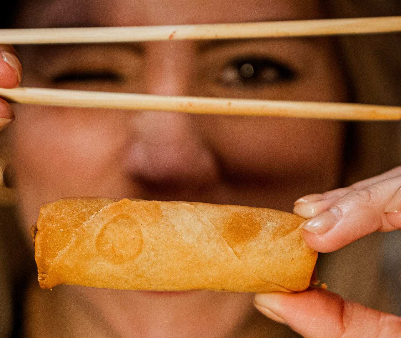 A diner holding a fried spring roll with wooden chopsticks, showing the crispy texture.