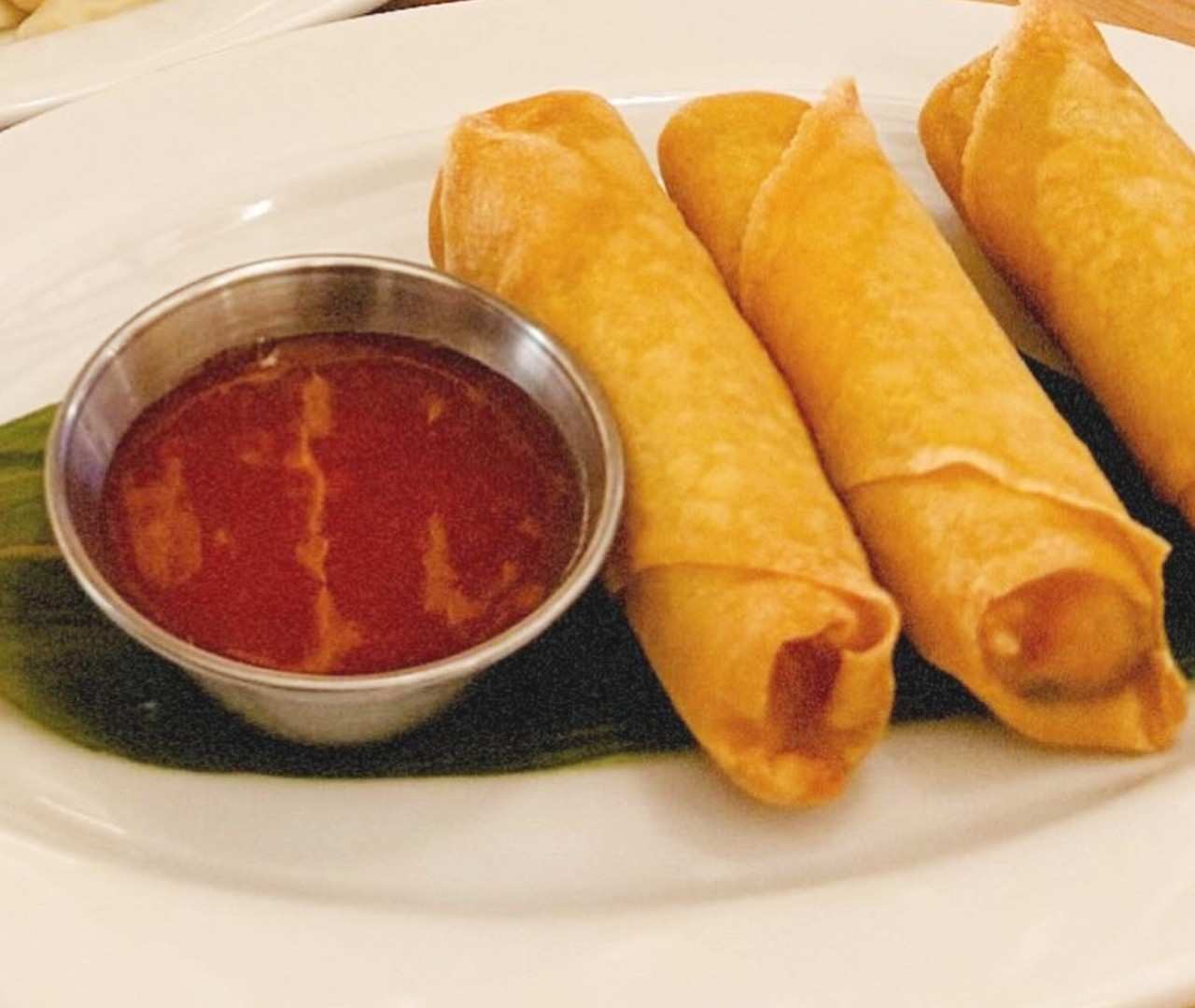Golden fried spring rolls served with a metal cup of sweet and sour dipping sauce.