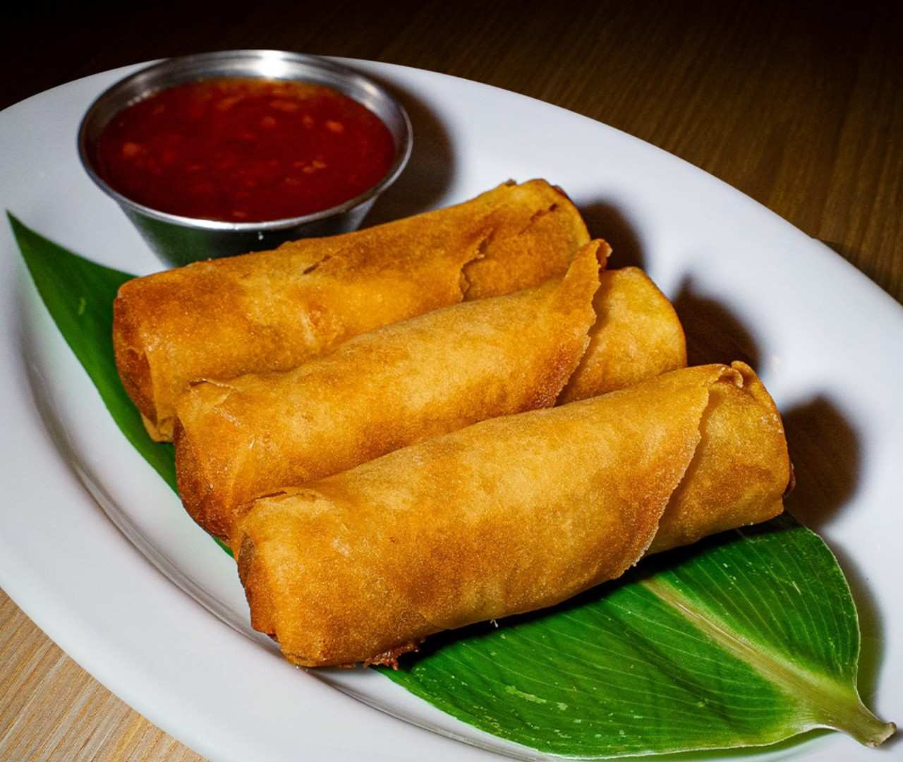 Elegant serving of three crispy spring rolls with sauce on a white oval plate.